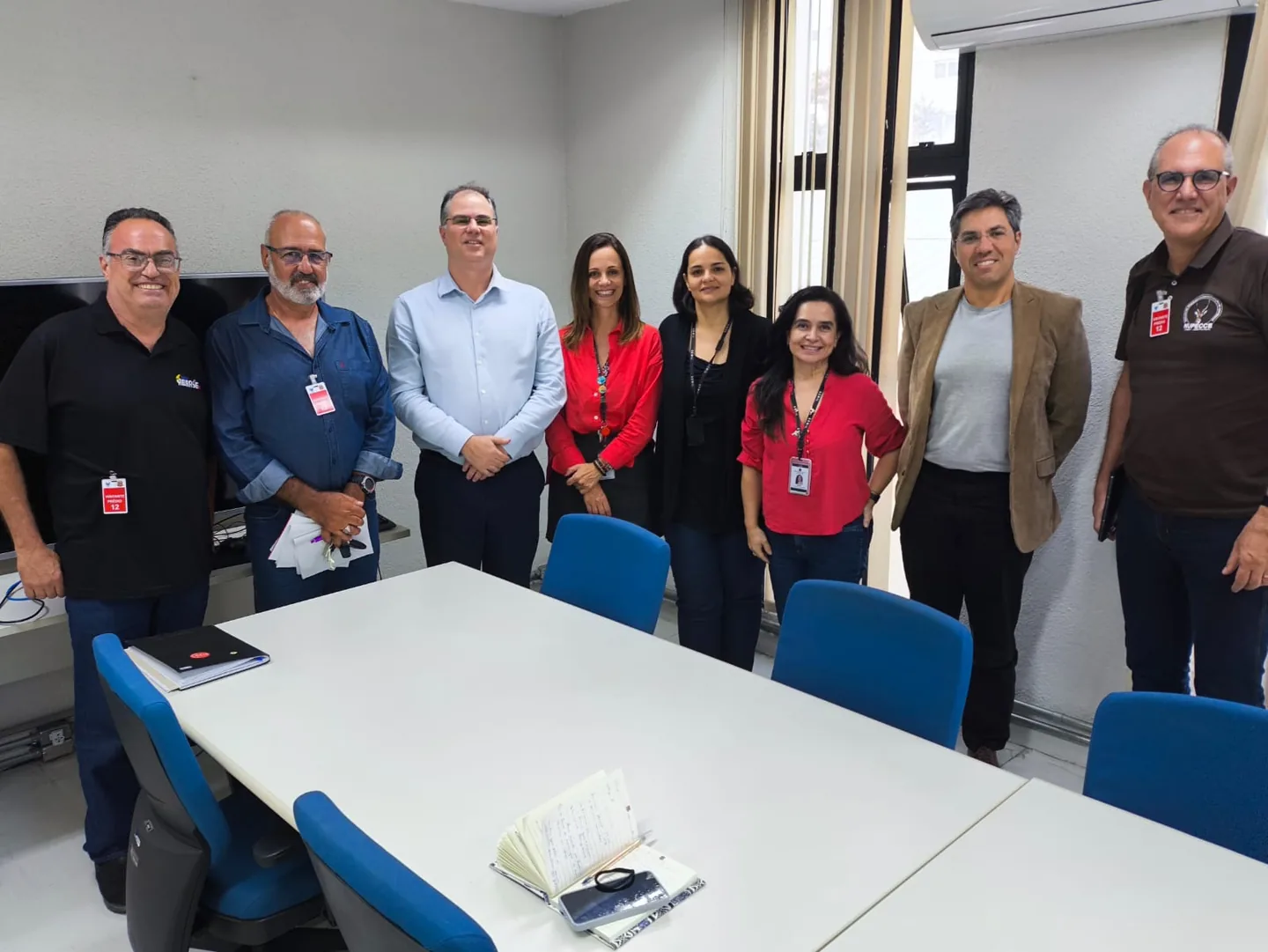 Oito pessoas em pé, lado a lado, junto a uma mesa de reunião na sede da SEMIL